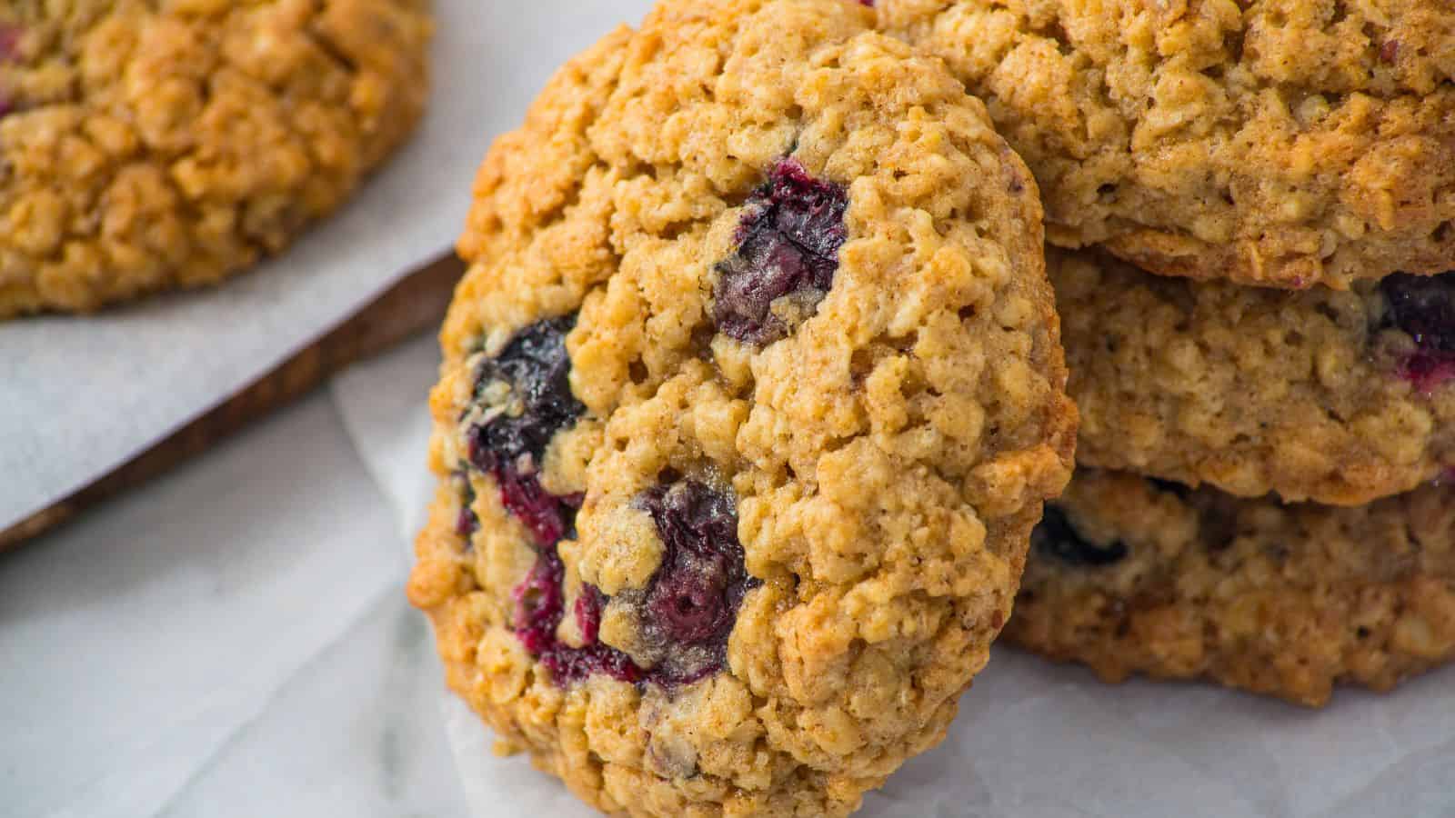 Close-up of oatmeal cookies with visible blueberries stacked on parchment paper.