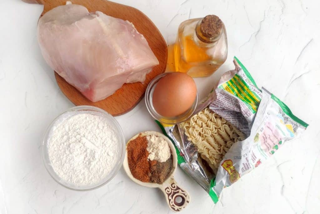 Ingredients for panko chicken nuggets  including chicken and eggs on a white counter.