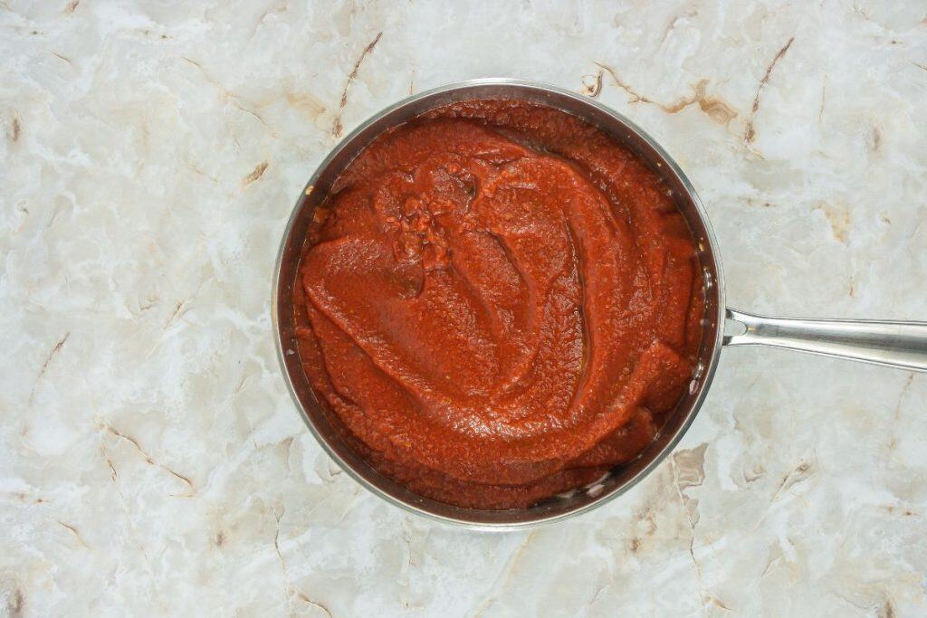 A saucepan filled with smooth red tomato sauce sits on a light-colored marble countertop.