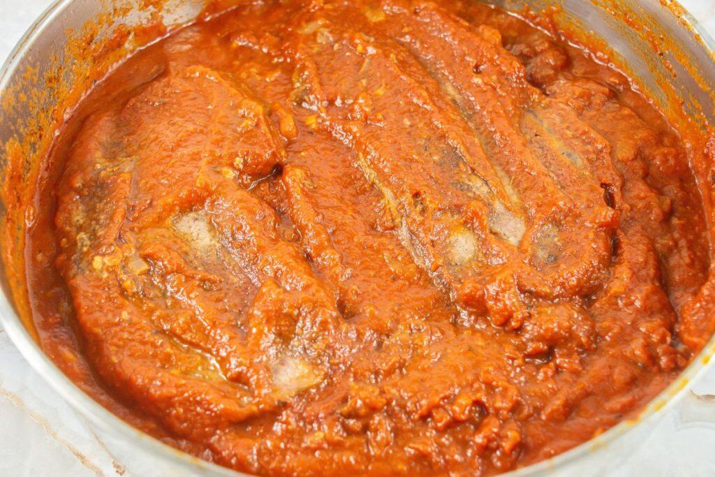 A close-up view of a pot filled with red tomato stew and fish pieces simmering in the sauce.