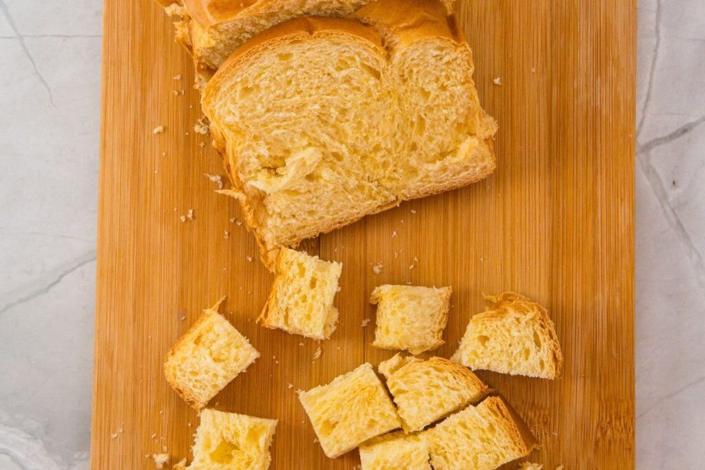Sliced bread and cubed bread pieces on a wooden cutting board.