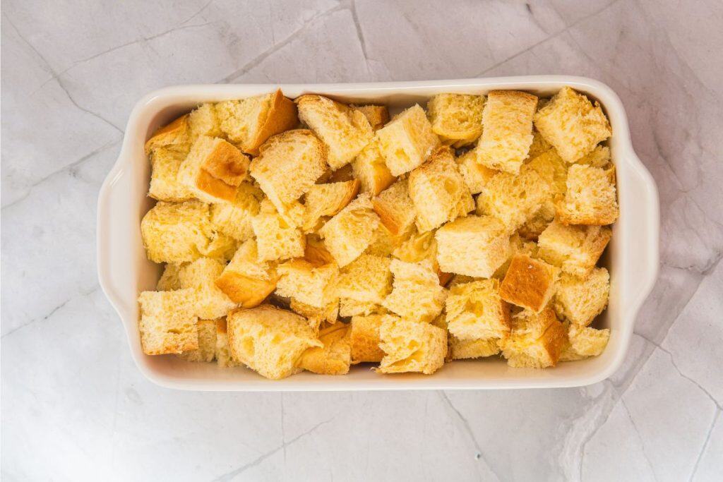 A rectangular baking dish filled with evenly cut cubes of bread on a light marble surface.