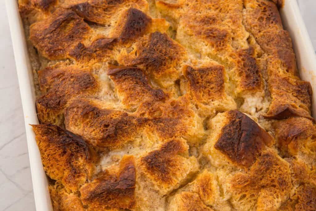 Golden-brown bread pudding with a crisp, textured top, baked in a white rectangular dish.