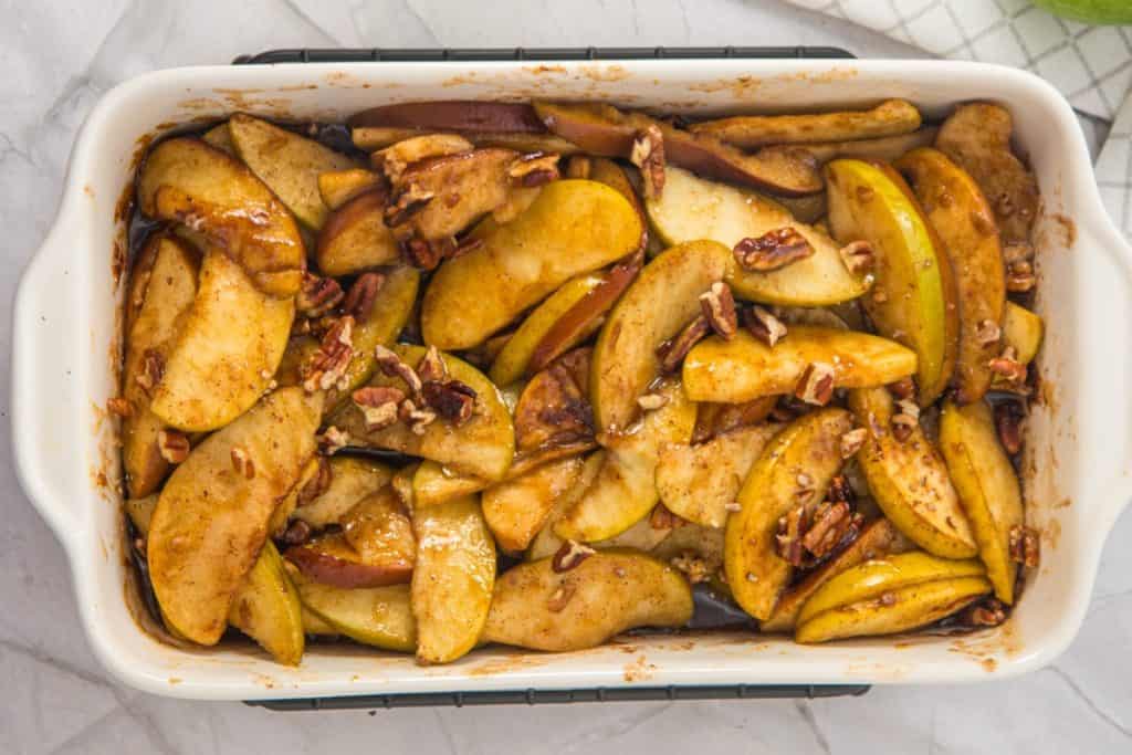 Sliced apples mixed with pecans, cinnamon, and spices arranged in a rectangular baking dish, ready to be baked.