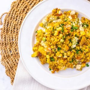 A white plate holds a serving of cornbread casserole with visible corn, green peppers, and herbs—similar in comfort to a Chicken Casserole with Stuffing Recipe—set on a woven placemat with a white napkin underneath.