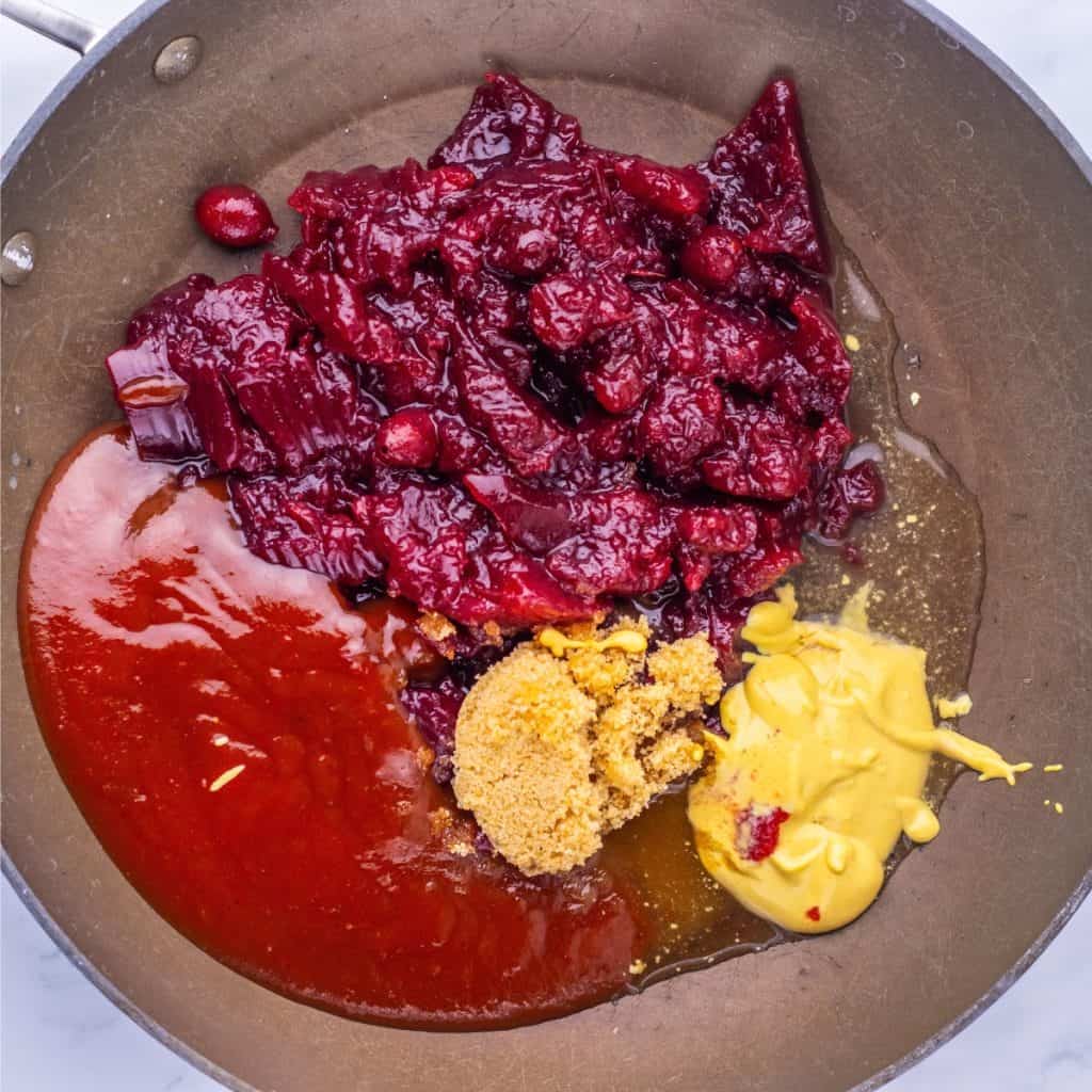 A pan containing cranberry sauce, yellow mustard, brown sugar, and barbecue sauce, all unmixed and arranged in separate sections—perfect for making cranberry glaze for turkey stuffing meatballs.