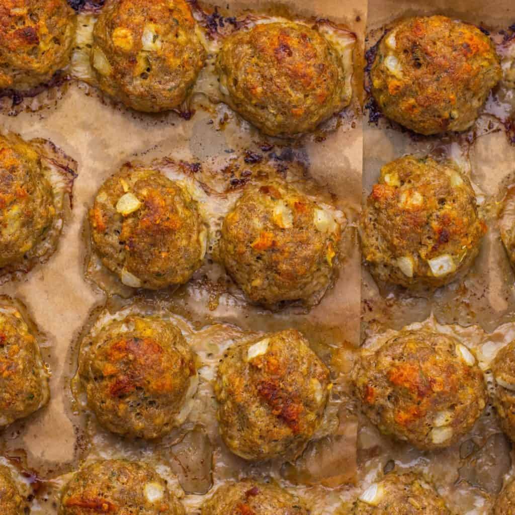 Turkey and Stuffing Meatballs cooking on a parchment-lined pan, featuring a browned, slightly crispy exterior with visible diced onions.