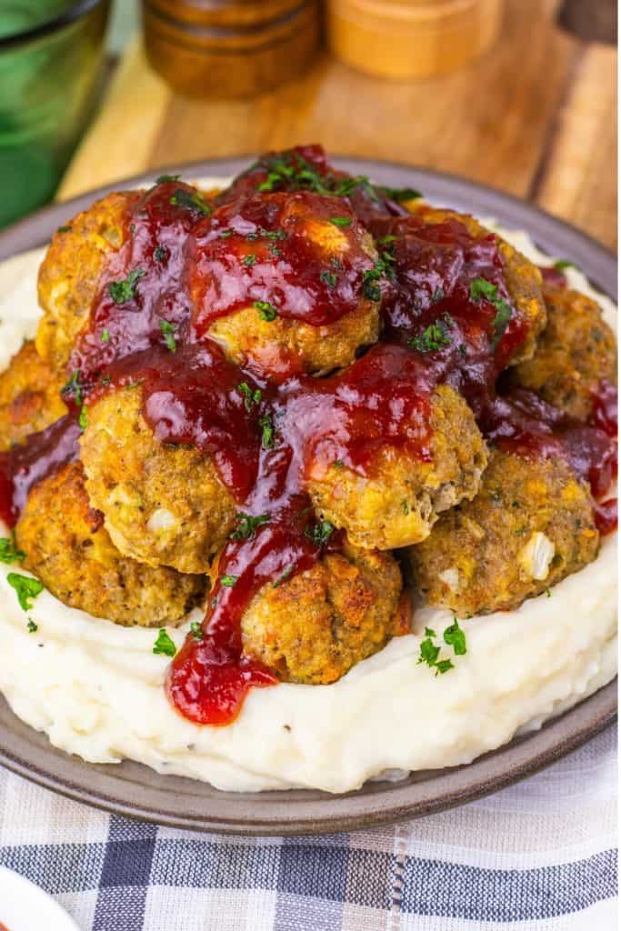 A plate of mashed potatoes topped with several meatballs covered in a red sauce, garnished with chopped parsley.