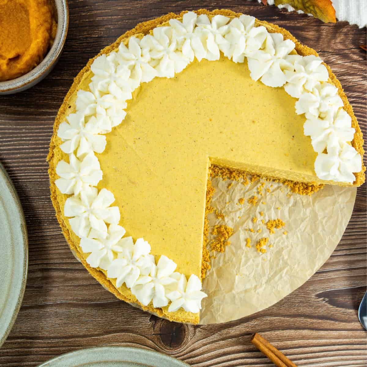 A no-bake pumpkin pie with a missing slice, decorated with a ring of piped whipped cream on a wooden surface.