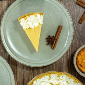 A slice of no bake pumpkin pie topped with whipped cream, served on a gray plate with a cinnamon stick and star anise.