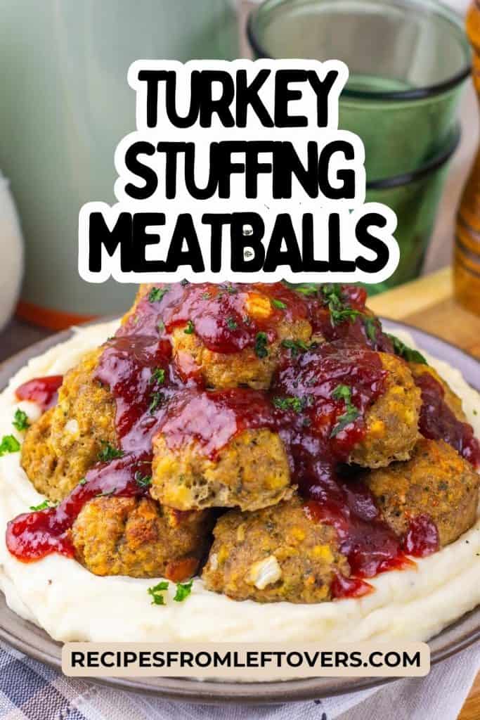 A plate of turkey stuffing meatballs with cranberry sauce is served on mashed potatoes, garnished with parsley. Two glass cups and a pepper grinder are in the background.